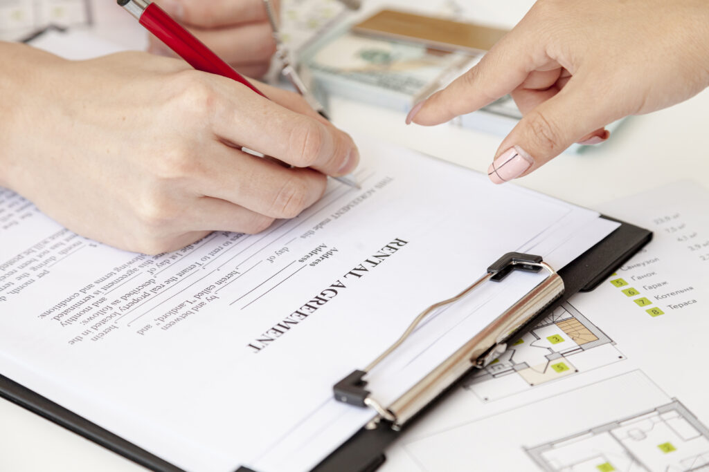 A legal professional and client finalizing a transaction by signing a rental agreement, placed on top of property documents.