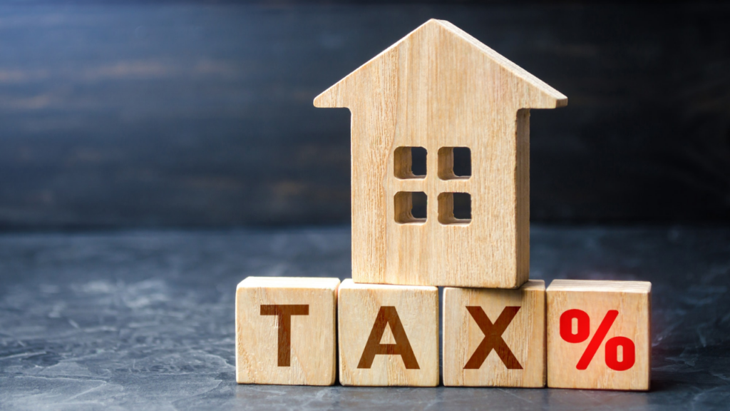 A small wooden house model sitting on blocks that spell out the word TAX.